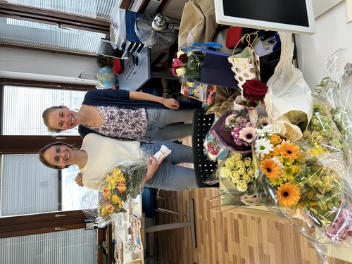 Daniela und ihre Nachfolgerin stehen vor einem Tisch mit vielen überreichten Blumen